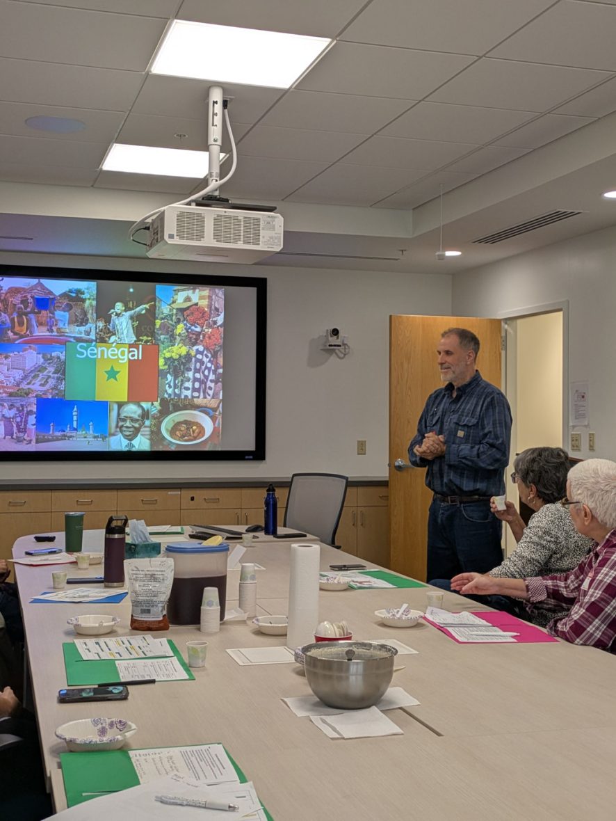 Presenter speaking to participants during a French immersion session with a presentation displayed on a screen.