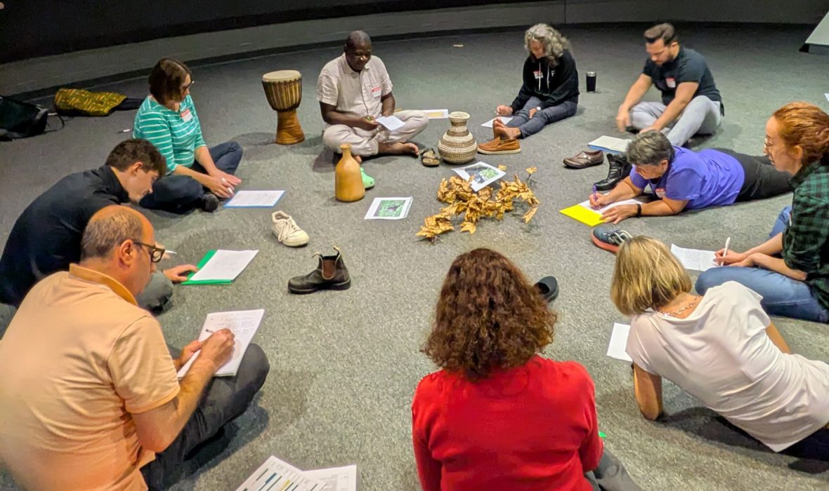 Participants seated in a circle during a cultural learning activity, writing notes and sharing discussion.