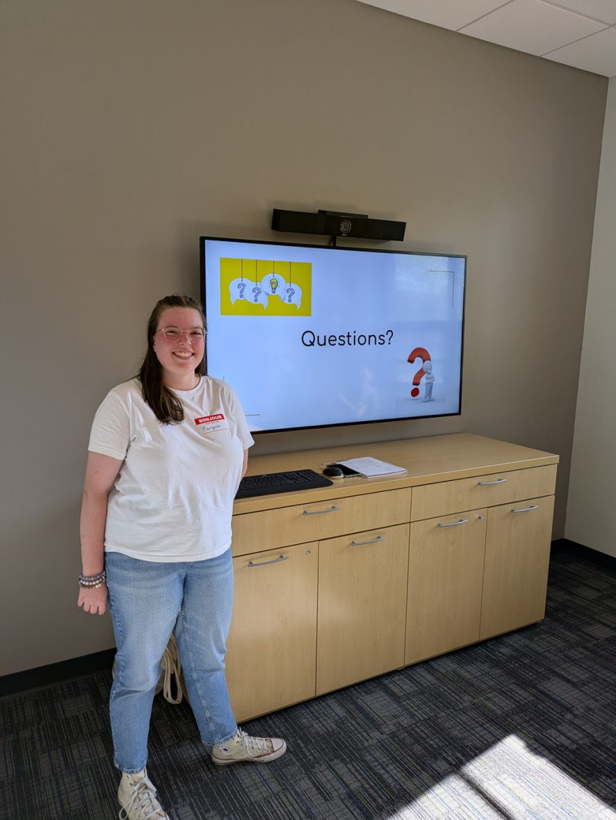 Presenter standing beside a display screen showing the final slide of a presentation.