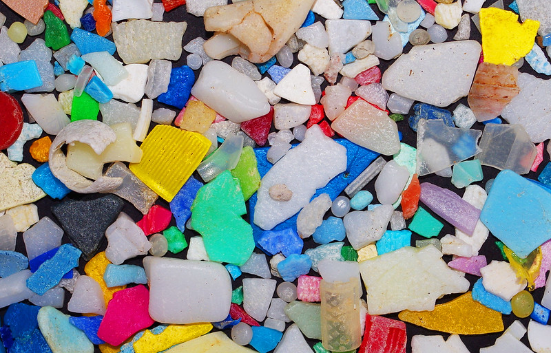 A photo of colorful plastics mixed with rocks on a shore.