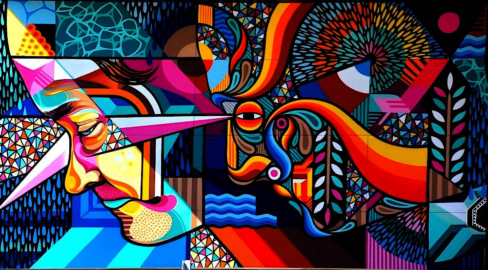 A mural depicting two abstracted faces in colorful shapes, gazing in the same direction toward the left of the frame.