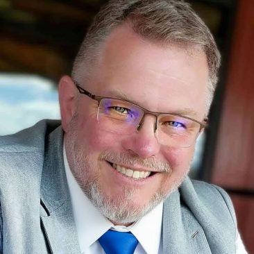 BJ Kitchin, with glasses, a gray blazer and blue tie.