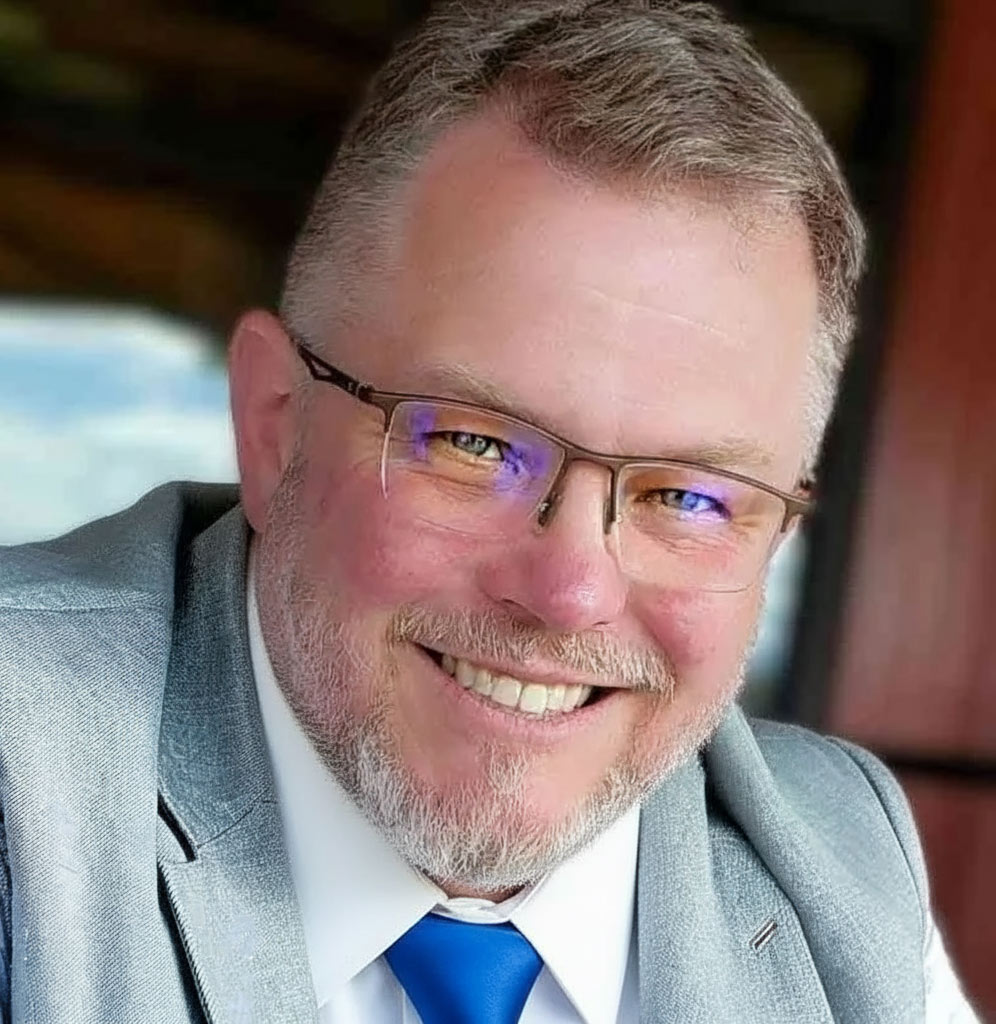 BJ Kitchin, with glasses, a gray blazer and blue tie.