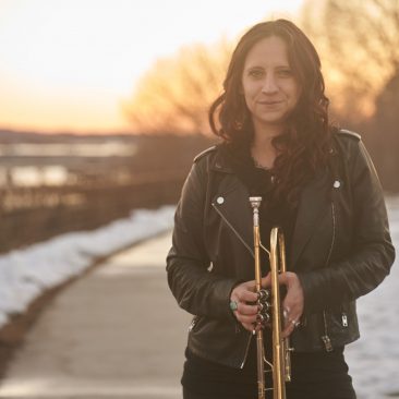 Emma Stanley poses outdoors with her trumpet and a sunset in the background