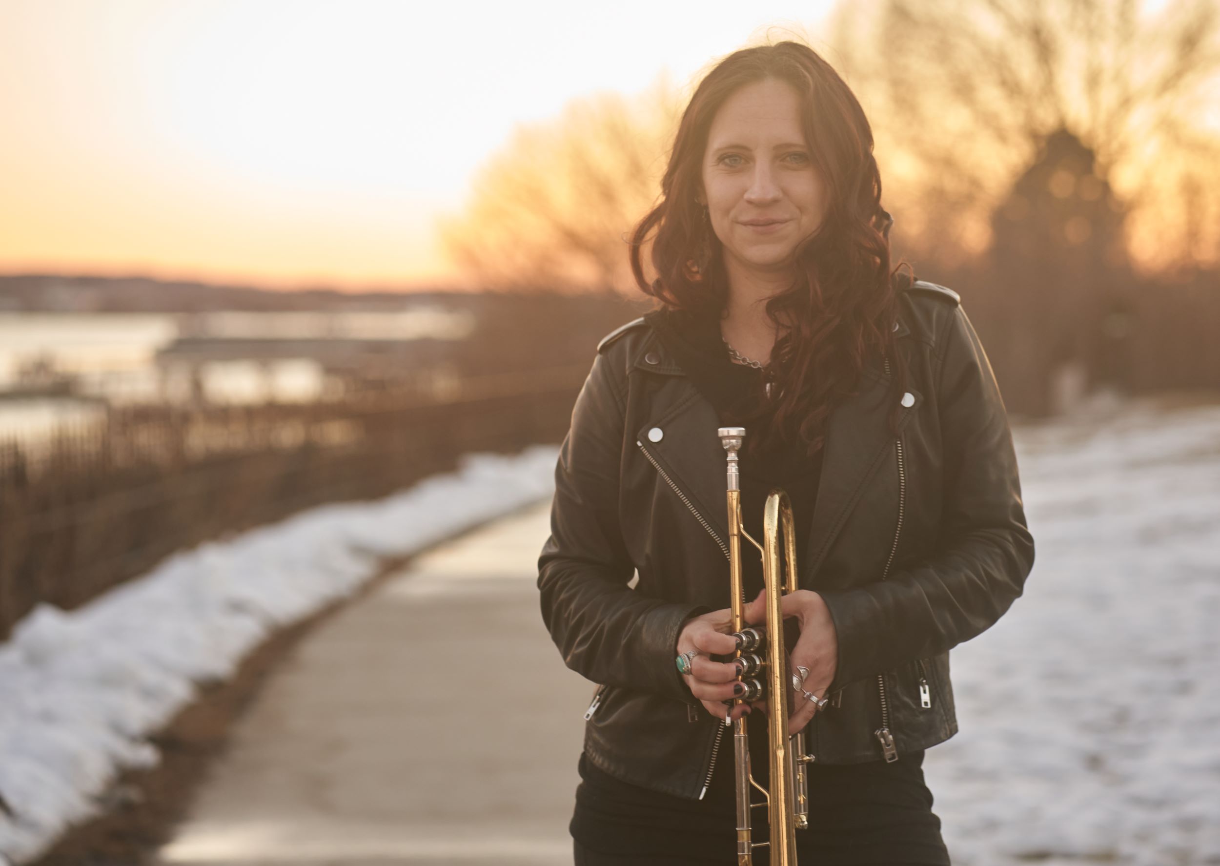 Emma Stanley poses outdoors with her trumpet and a sunset in the background