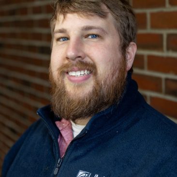 headshot of edward hess, wearing a dark blue uma branded fleece sweater.