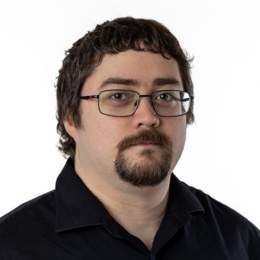 Professional headshot of Kendall Wilcox, a man with short brown hair, brown eyes, goatee, and glasses