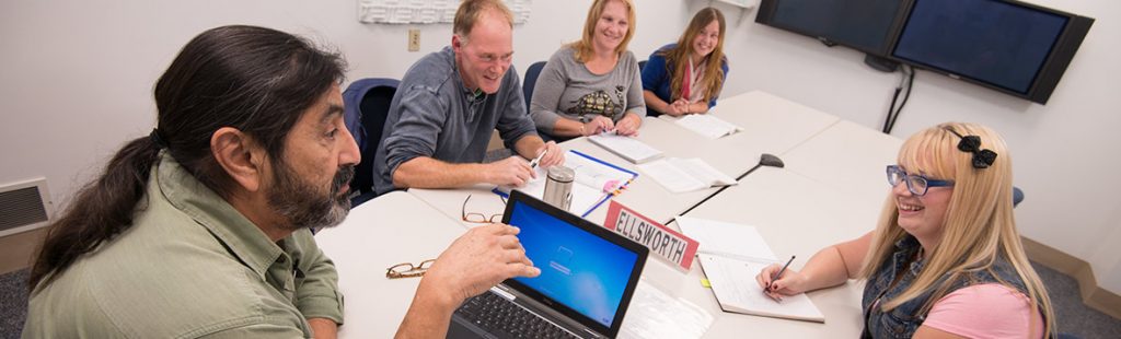 An instructor is in discussion with students in a videoconference classroom.