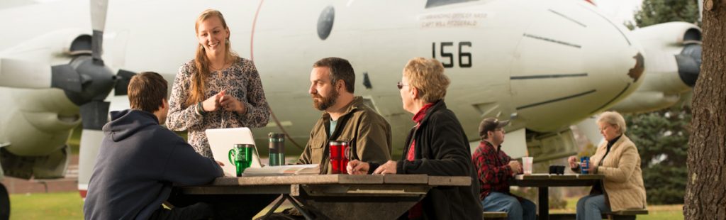 UMA Brunswick Center - students sitting at a picnic table next to the iconic planes on Brunswick Landing