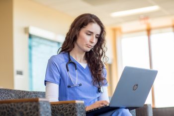 UMA nursing student works on her laptop whie in scrubs at Maine General Hospital