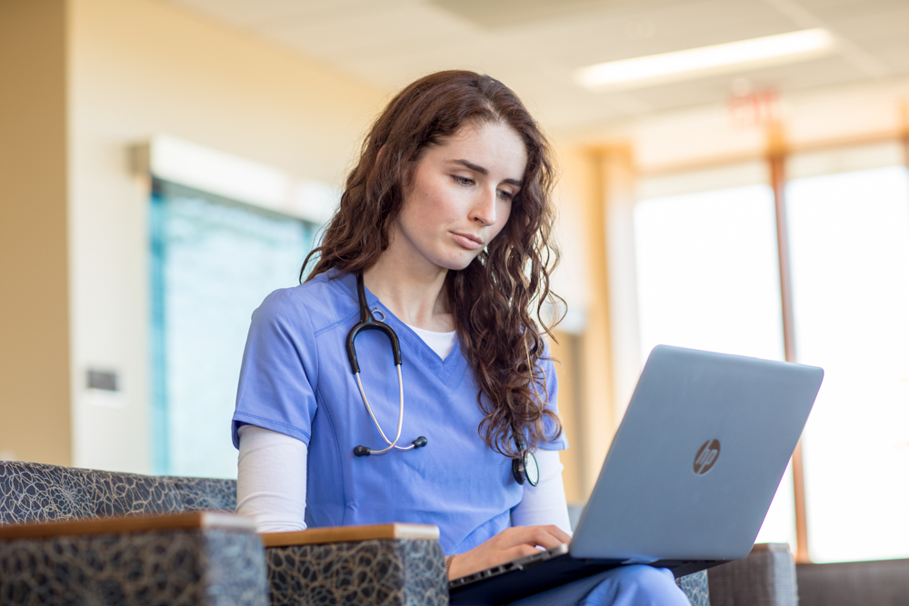 UMA nursing student works on her laptop whie in scrubs at Maine General Hospital