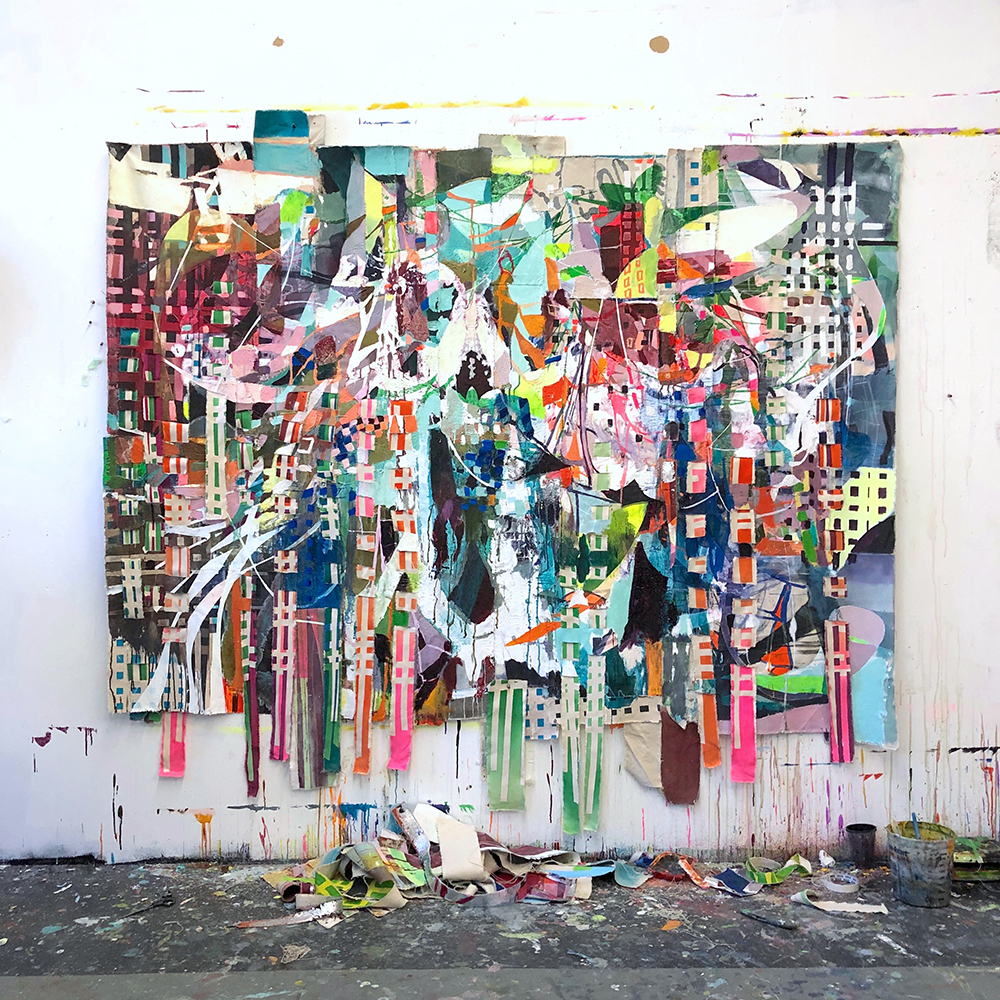 The image is a studio view of Galen Cheney's large painting "Interpreter of Dreams" that shows the painting pinned against a white wall with stray paint lines on it, and a dark gray paint-splattered floor below. "Interpreter of Dreams" is very colorful painting with gridded and gesturally-painted strokes of fluorescent pink, yellow, and orange paint among many other shades of blue, green, red, and white, that is also literally interwoven with painted strips of canvas that weave through the painting's surface. There is not any central image in the painting, but a cacophony of color and line that is bold, energetic, and colorful. The woven strips of painted canvas hang down below the painting's edge.
