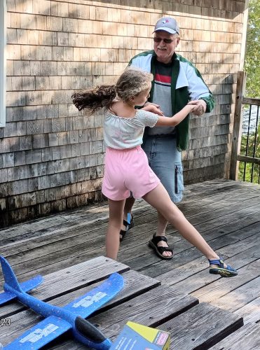 a man and a young girl dancing on a wood deck