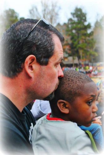 a Caucasian man gently kissing a young boy with dark skin on the head