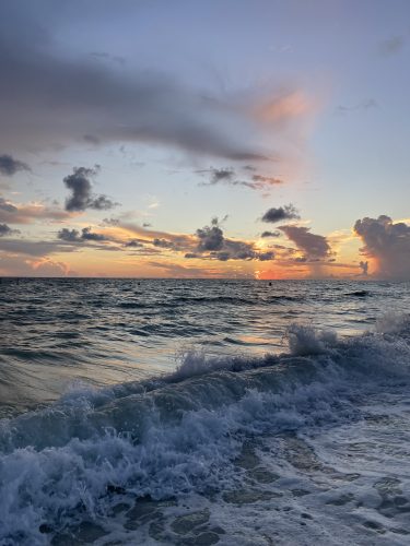 a ocean scene of waves and a light blue orange sky with clouds