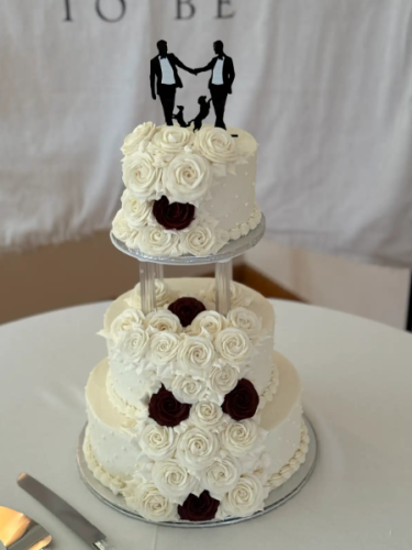a two-tiered wedding cake with a topper of two dogs and two men holding hands 