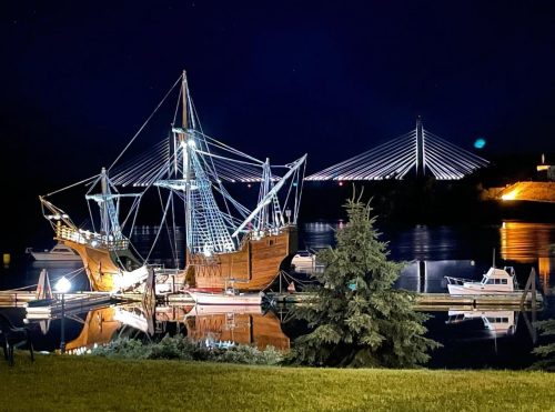 a lighted clipper ship on a river with a illuminated suspension bridge in the background
