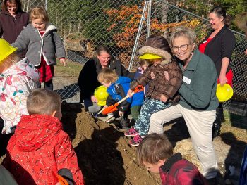 Deb Rountree and a group of kids in winter coats happily playing in a big pile of sand