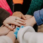 a diverse group reaching their hands all into the center of the group