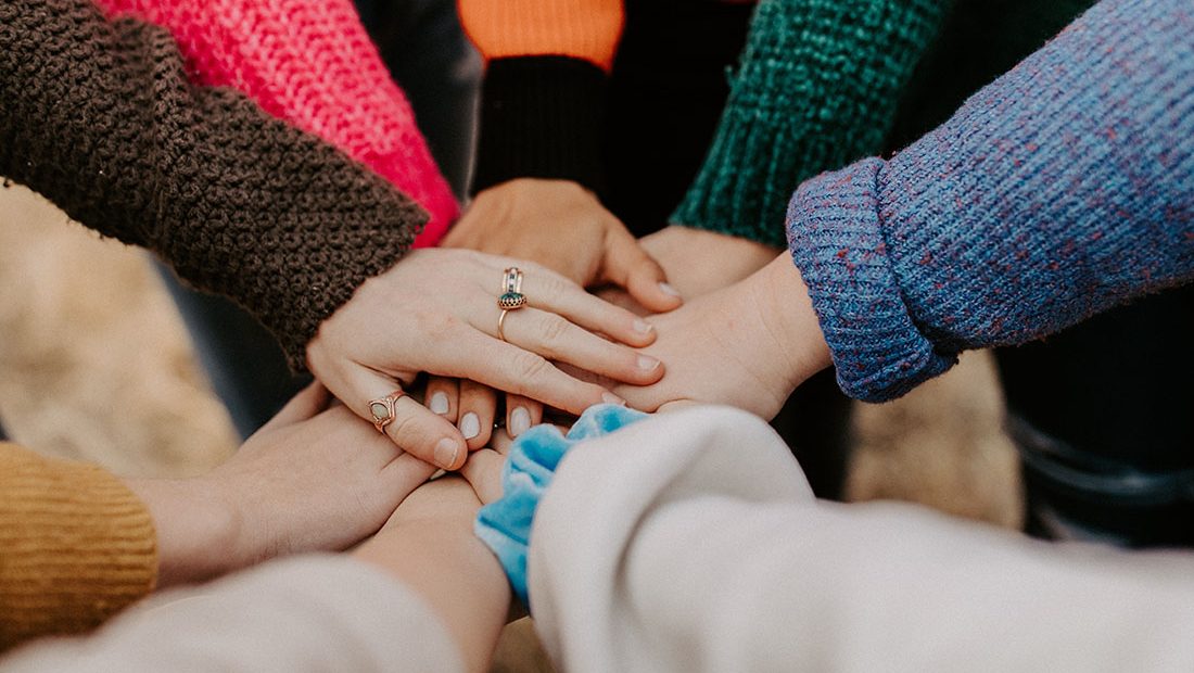 a diverse group reaching their hands all into the center of the group