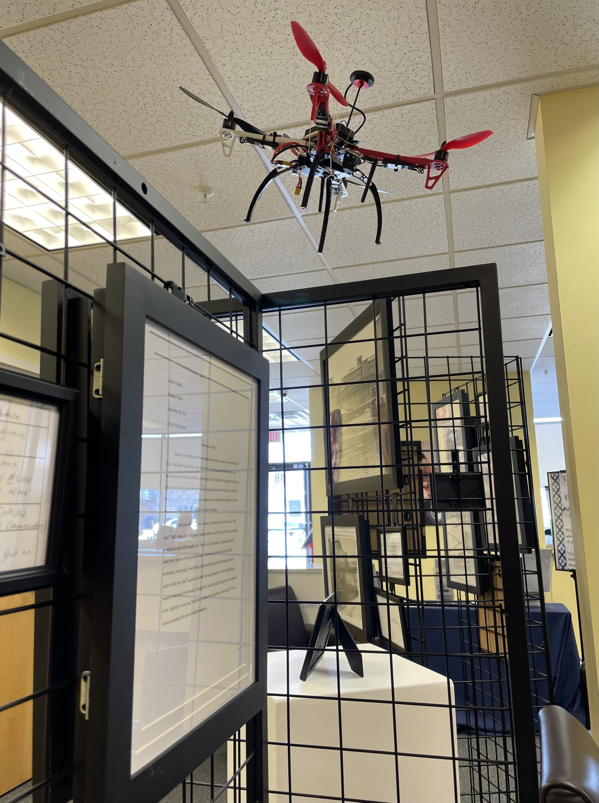 A drone created by a UMA Student hangs over a display of other student work.