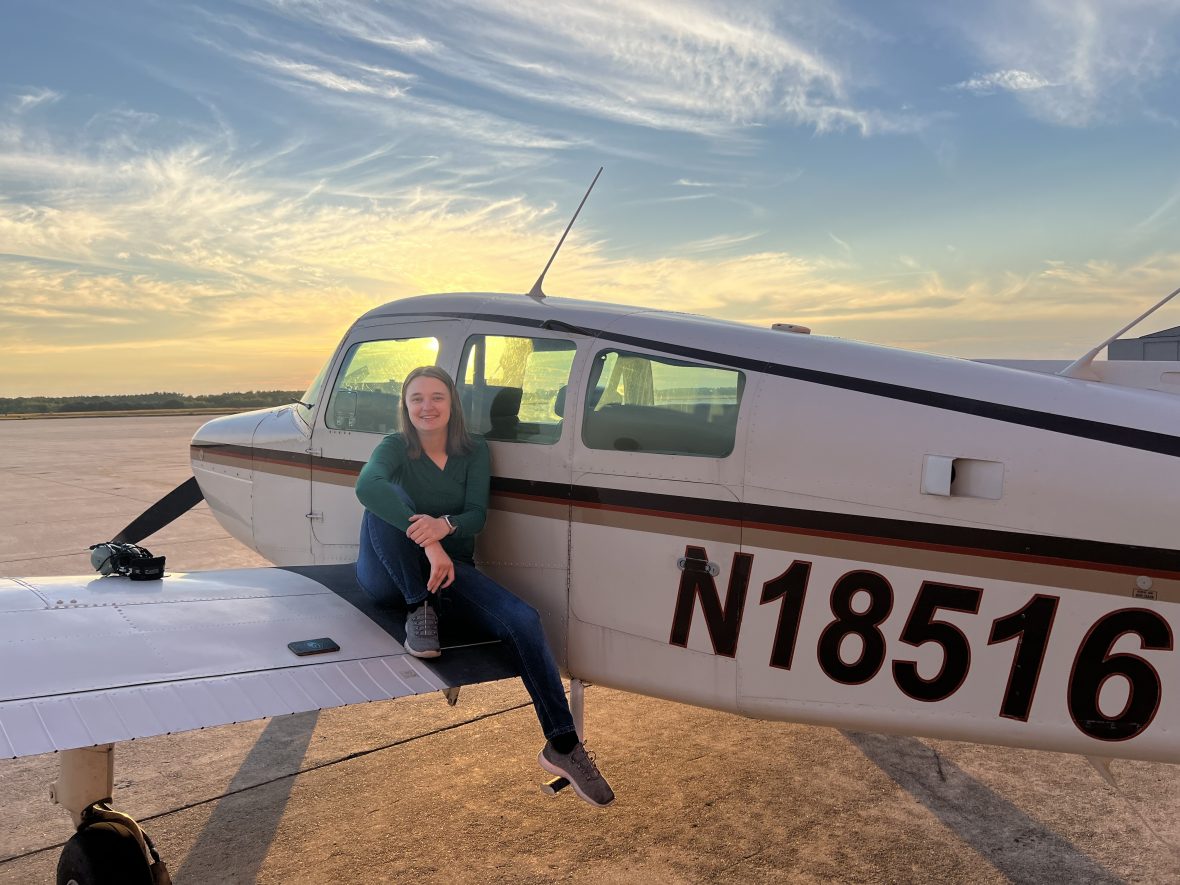 Casey Raymond sits on the wing of an airplane with a sunset in the background.