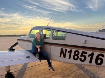 Casey Raymond sits on the wing of an airplane with a sunset in the background.
