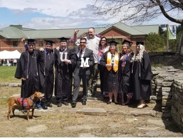 Graduates wearing graduation caps and gowns with red, white and blue honor cords pose for a group picture