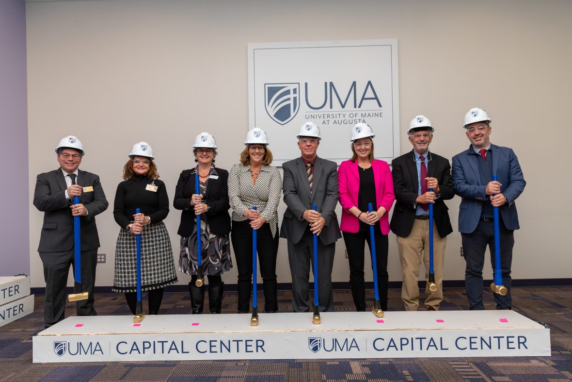 University of Maine at Augusta leaders and community partners pose wearing hardhats and safety glasses while holding sledge hammers to celebrate the groundbreaking of the new UMA Capital Center.