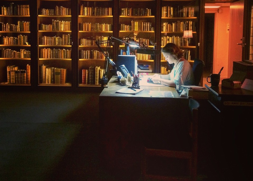a person studying at a desk in a dimly lit library with a bright desk lamp
