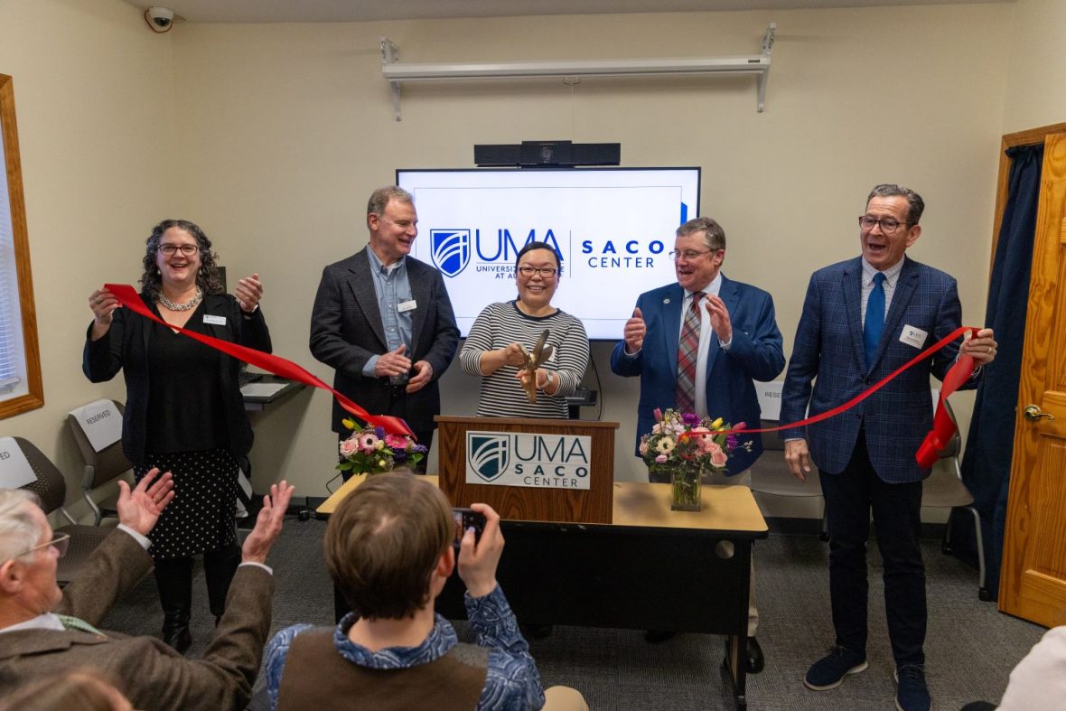 Five people stand with a large ribbon as the center person cuts it with large scissors in celebration of UMA Saco Center’s new location
