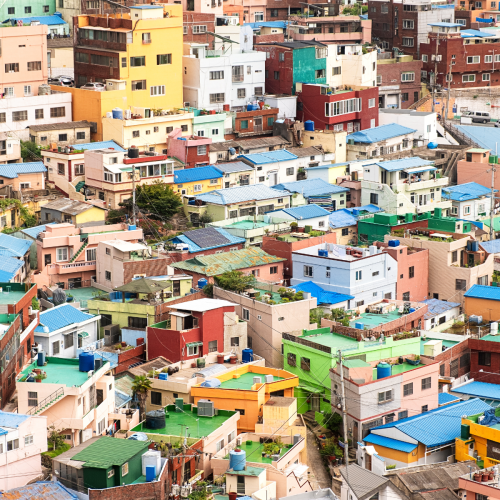 A densely packed hillside of colorful, multi-story buildings with bright blue roofs, in an urban coastal setting.
