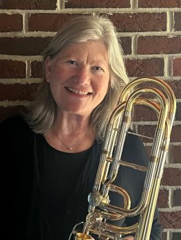 Anita Jerosch smiles and poses with her trombone in front of a brick wall
