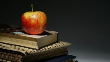 shiny red apple atop a stack of textbooks