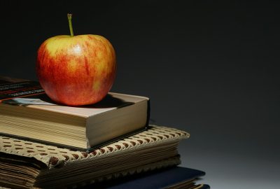 shiny red apple atop a stack of textbooks