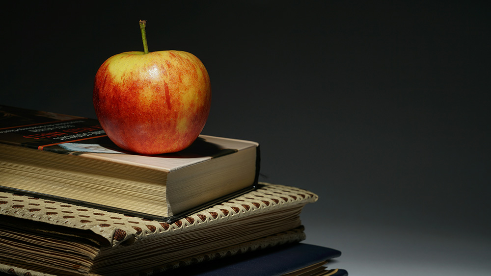 shiny red apple atop a stack of textbooks