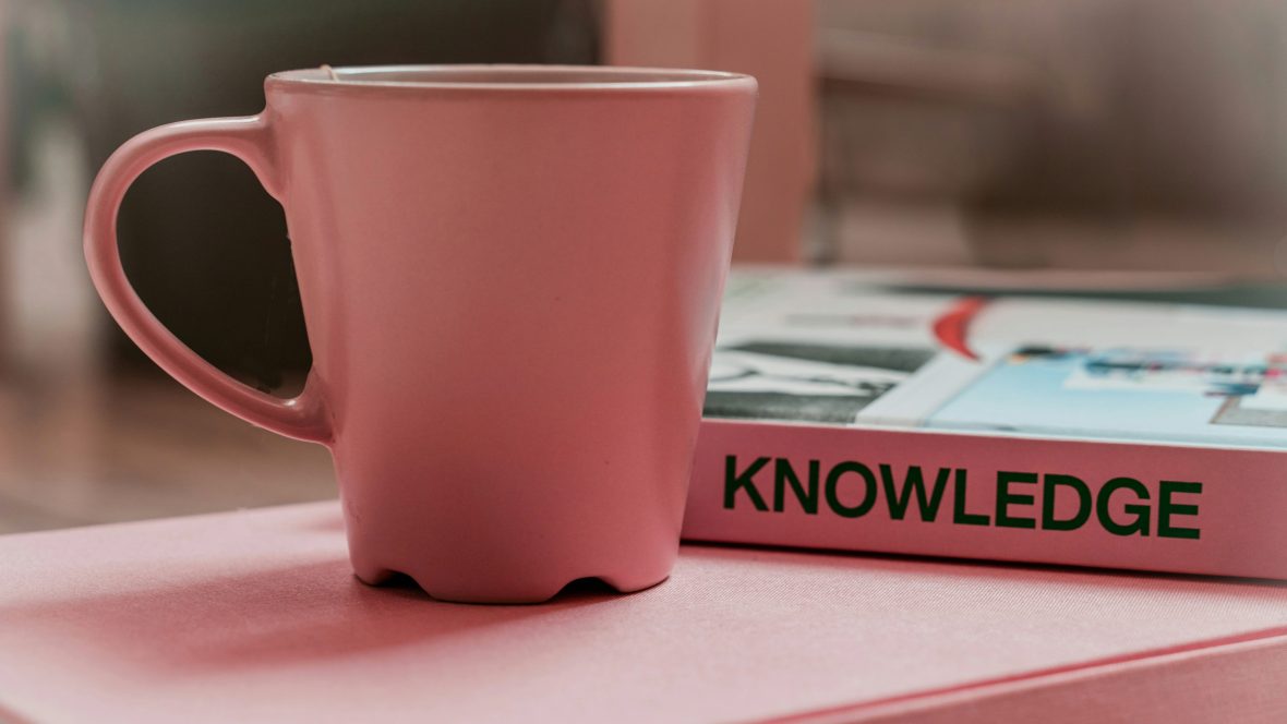 A pink cup next to a pink book titled "KNOWLEDGE"