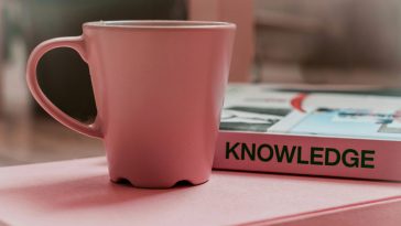 A pink cup next to a pink book titled "KNOWLEDGE"