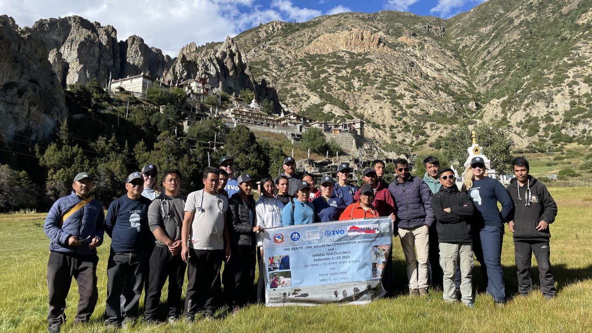 A group of local Nepalese animal care professionals and IVO instructors hold a banner. Large mountains in the background.