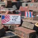 A painted brick with an american flag that reads "Land that I love. 9/11. This is my country. These are my people. I remember."