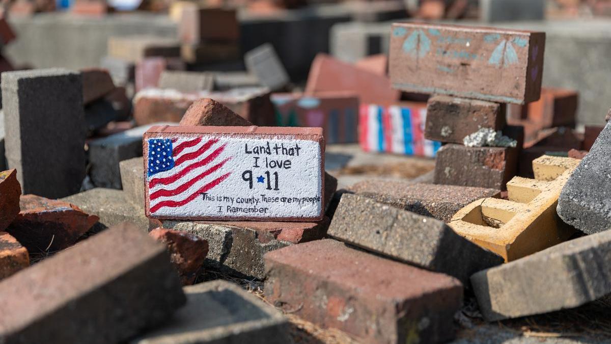 A painted brick with an american flag that reads "Land that I love. 9/11. This is my country. These are my people. I remember."