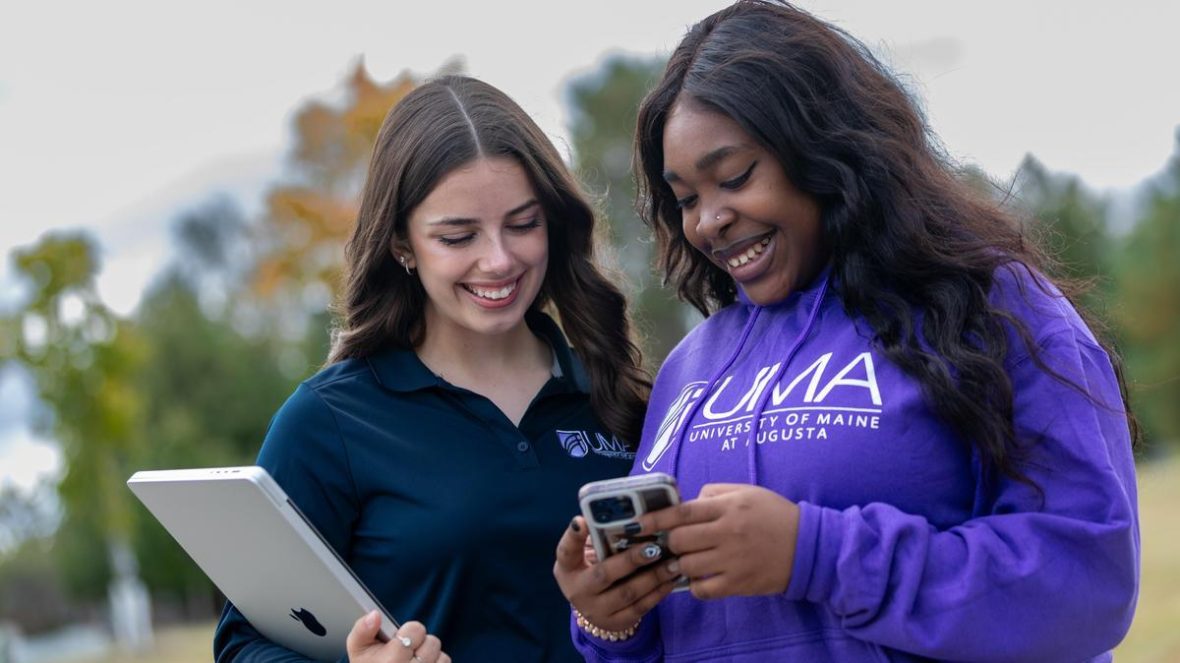 two UMA students texting on a smart phone