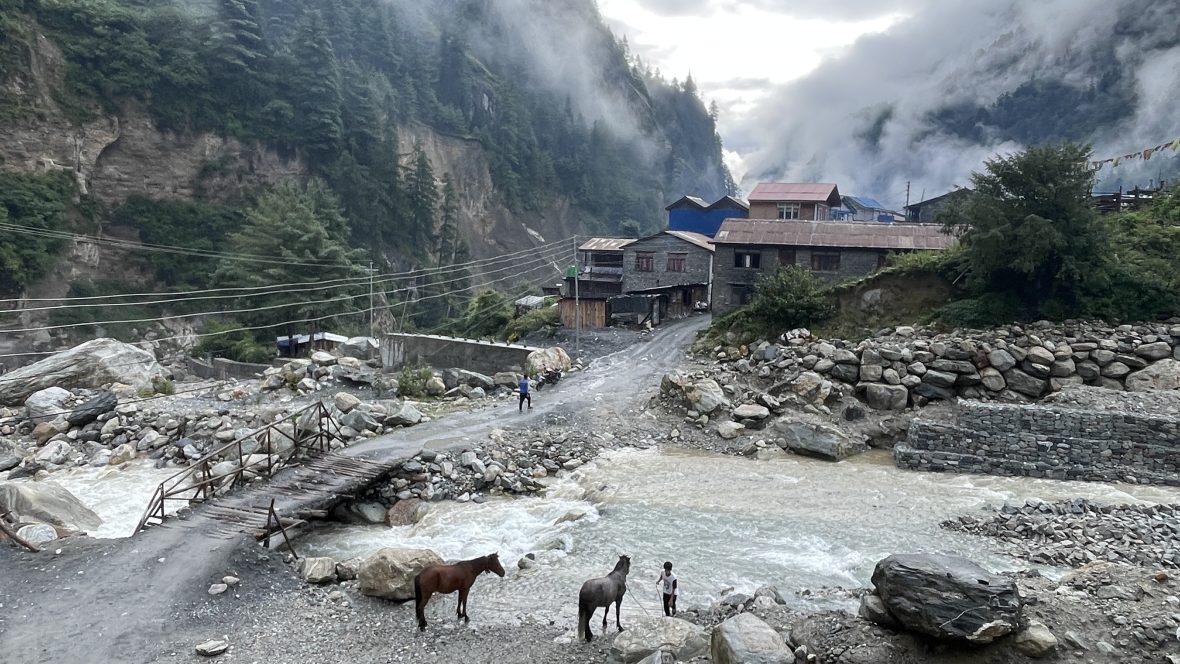 A village tucked in the Nepalese mountains with a narrow dirt road and rushing river