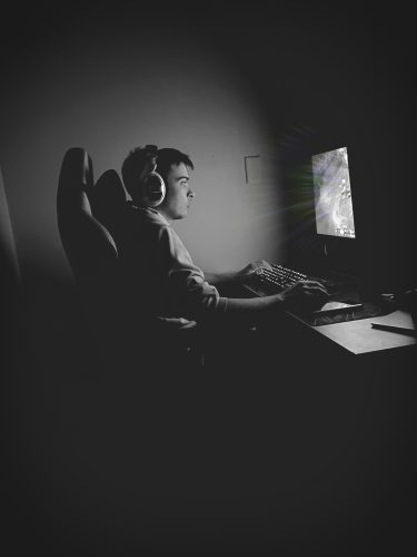 a monochromatic image of a man sitting at a desk facing a computer keyboard and monitor
