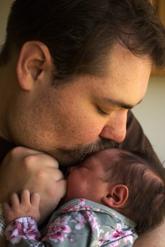 a man with a mustache kissing the forehead of a newborn baby