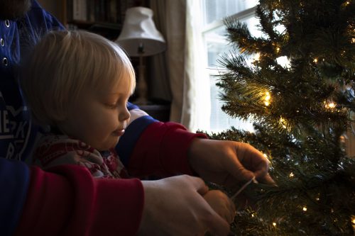 An adult assisting a young child to place an ornament on a Christmas tree 