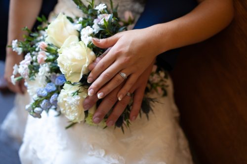 Close-up of two hands resting on a wedding bouquet of white roses and blue delphiniums.