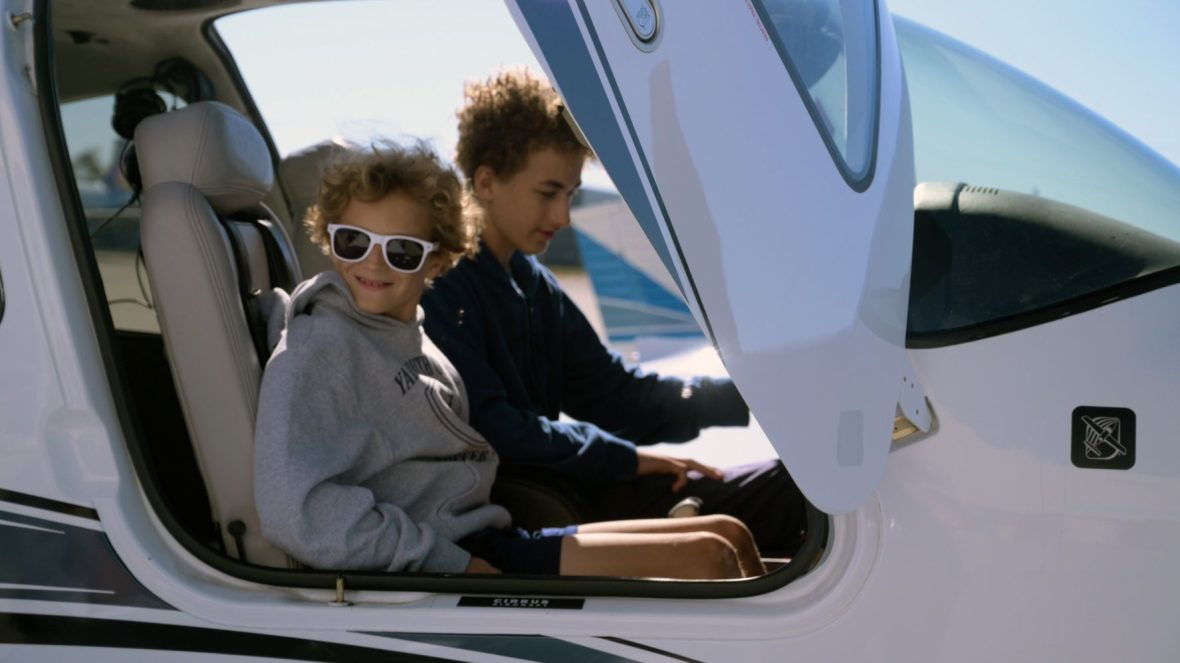 Two smiling children sit in the cockpit of a small airplane