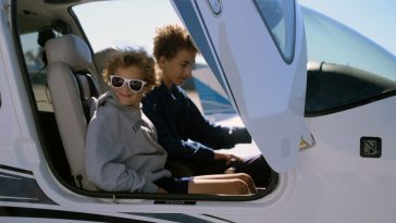 Two smiling children sit in the cockpit of a small airplane