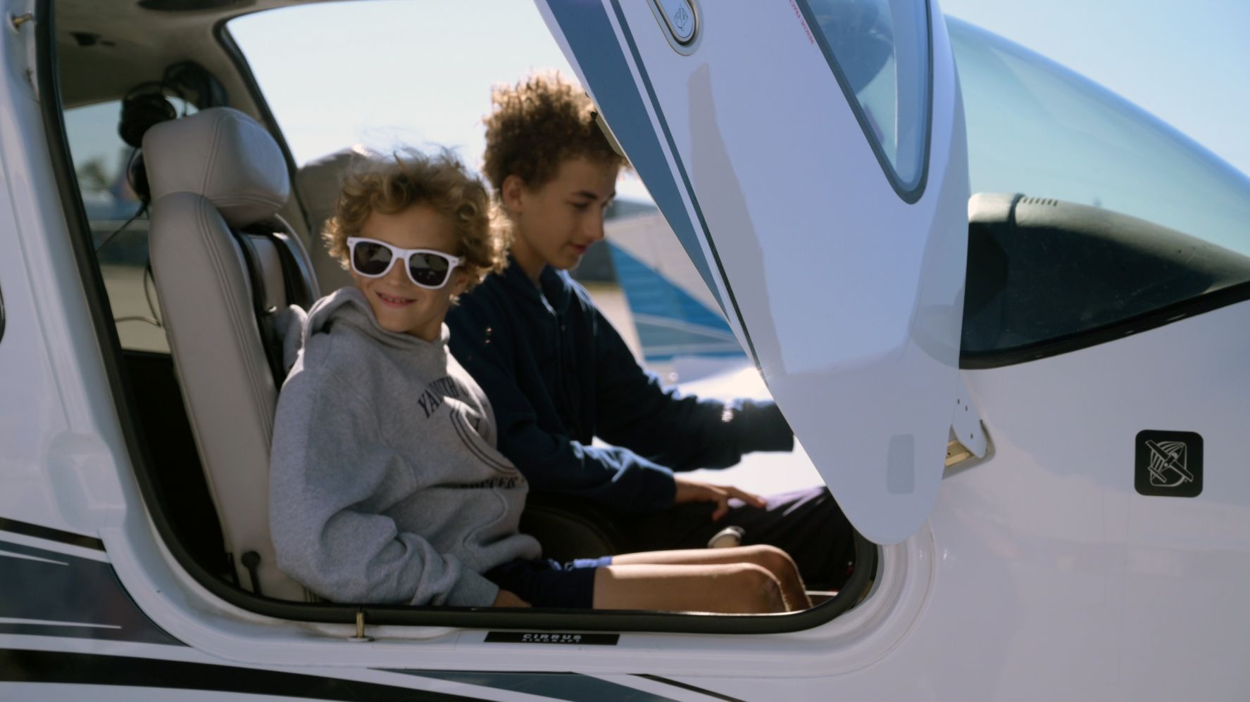 Two smiling children sit in the cockpit of a small airplane